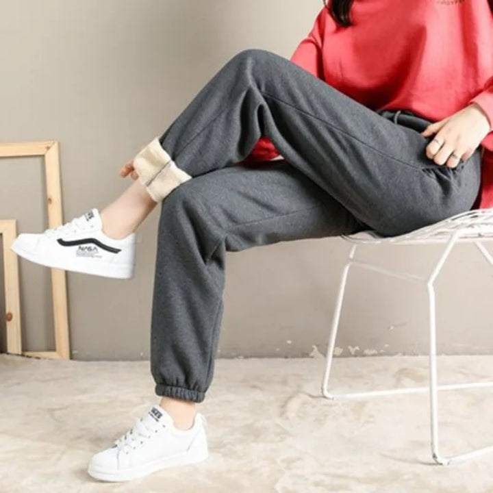 Stylish woman wearing winter fleece pants in gray with casual sneakers on a chair.